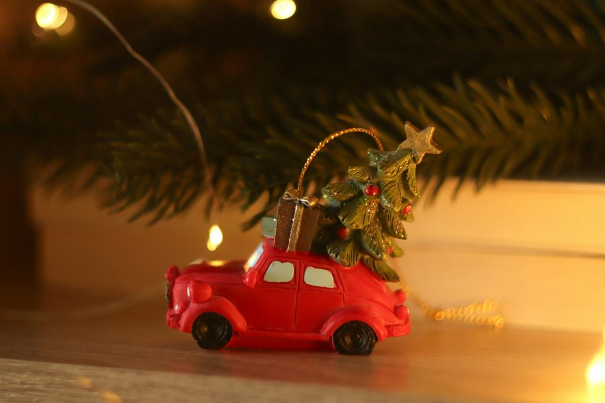 Rotes Spielzeugauto mit kleinem Weihnachtsbaum auf dem Dach im warmen Licht einer Lichterkette