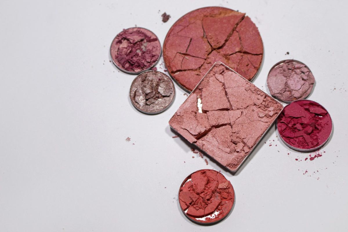 Zerbrochene Lidschatten- und Rouge-Pfännchen in Rosa- und Beerentönen auf weißem Grund
