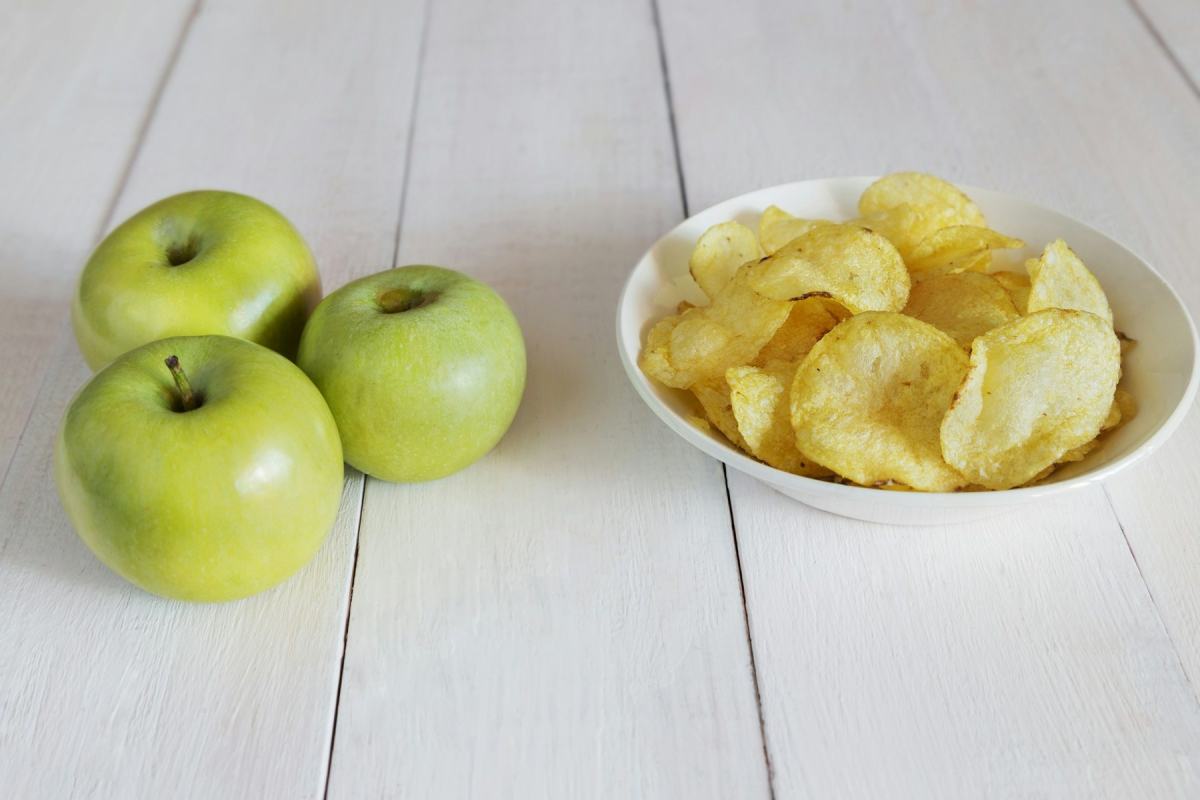 Schale mit Kartoffelchips neben grünen Äpfeln auf hellem Holztisch