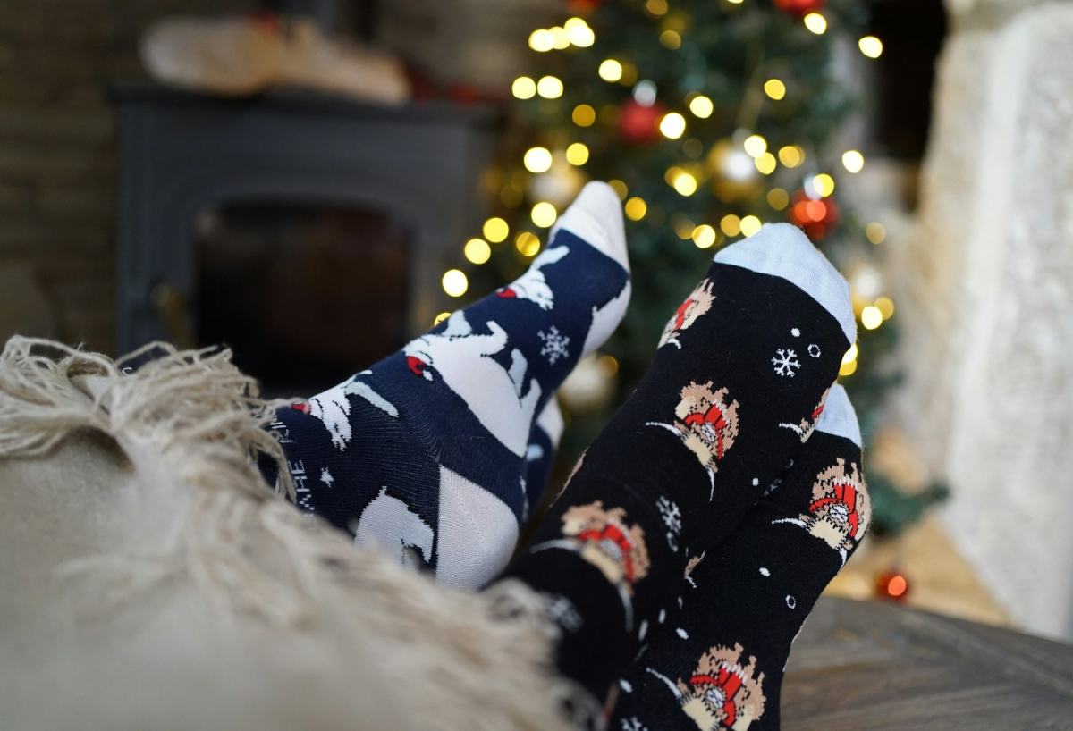 Füße in Wintersocken vor einem Kaminofen, im Hintergrund ein Weihnachtsbaum