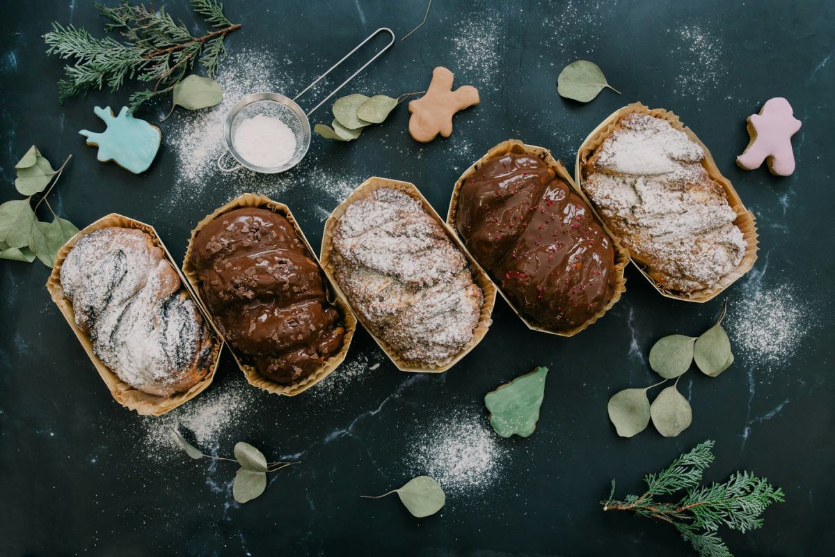 Fünf Christstollen mit Puderzucker auf dunklem Grund, umgeben von Eukalyptuszweigen