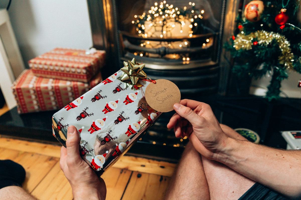 Hände halten ein verpacktes Geschenk mit Anhänger vor einem Kaminofen