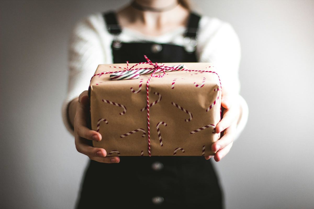 Person hält ein in Packpapier eingeschlagenes Geschenk mit rot-weißer Kordel