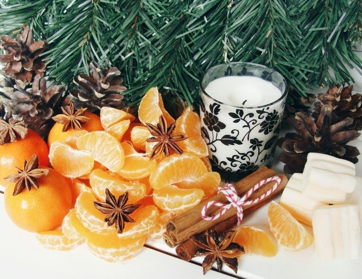 Mandarinenspalten, Sternanis und Zimtstangen neben einer Kerze und Tannenzapfen
