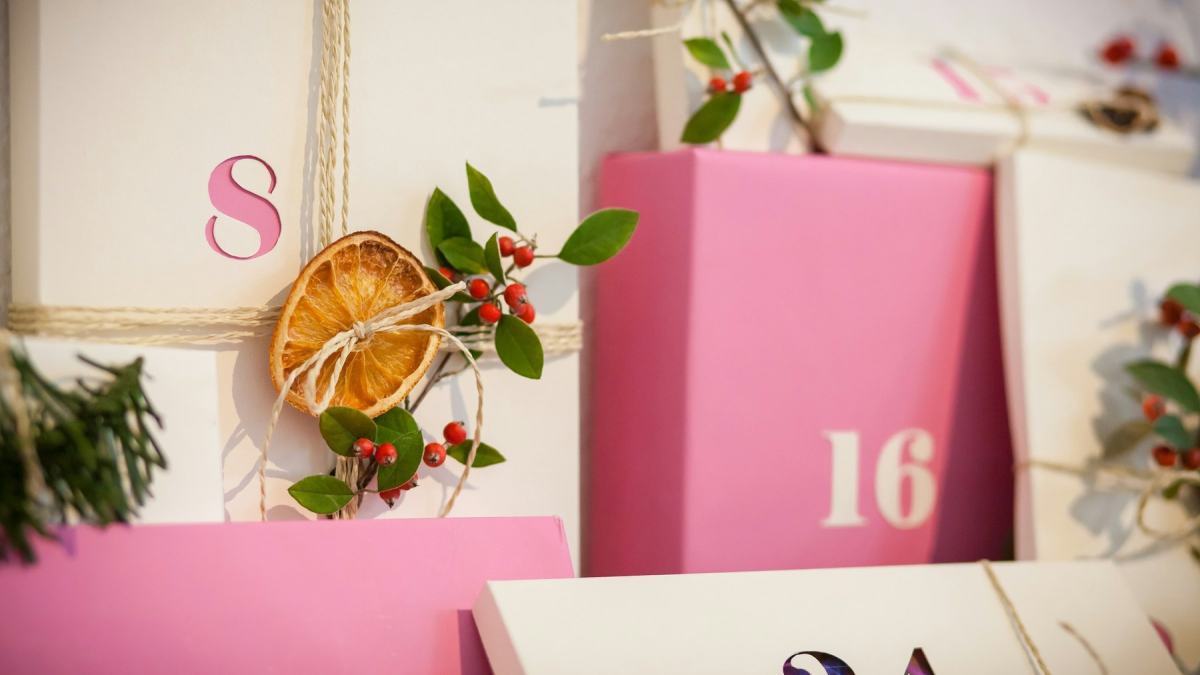 Adventskalender aus cremefarbenen und rosa Schachteln mit Zahlen, getrockneten Orangenscheiben und Ilex