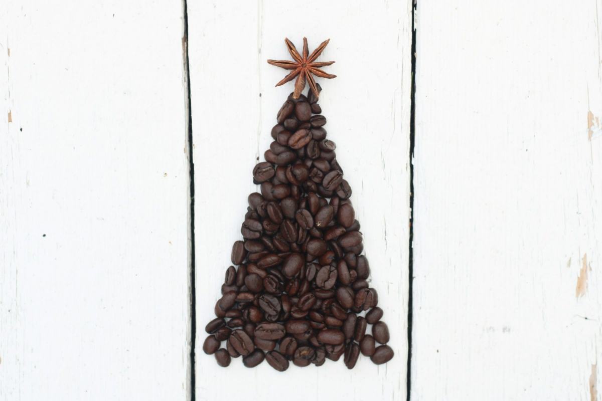 Kaffeebohnen, zu einem Tannenbaum gelegt, mit Sternanis als Spitze auf weißem Holz