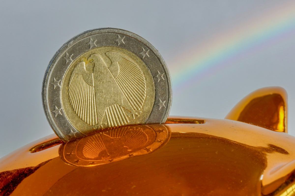 Euromünze steckt im Schlitz eines goldenen Sparschweins