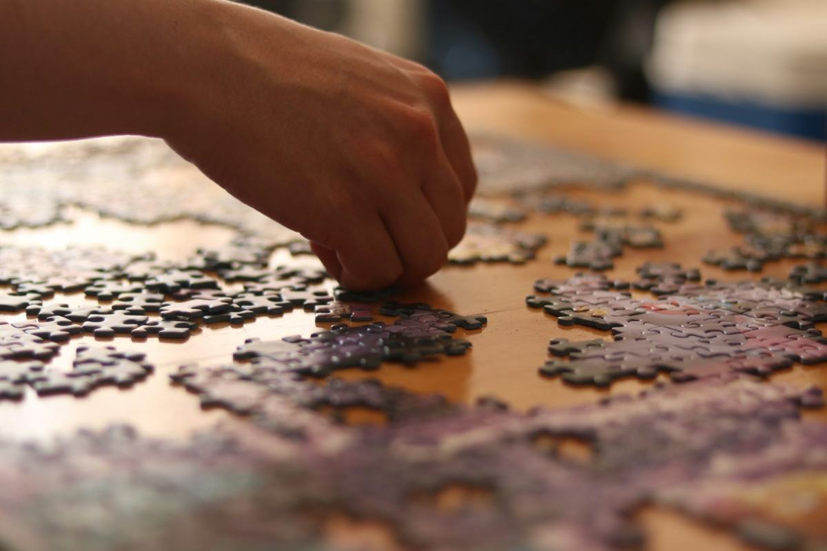Hand legt Puzzleteile auf einem Holztisch zusammen