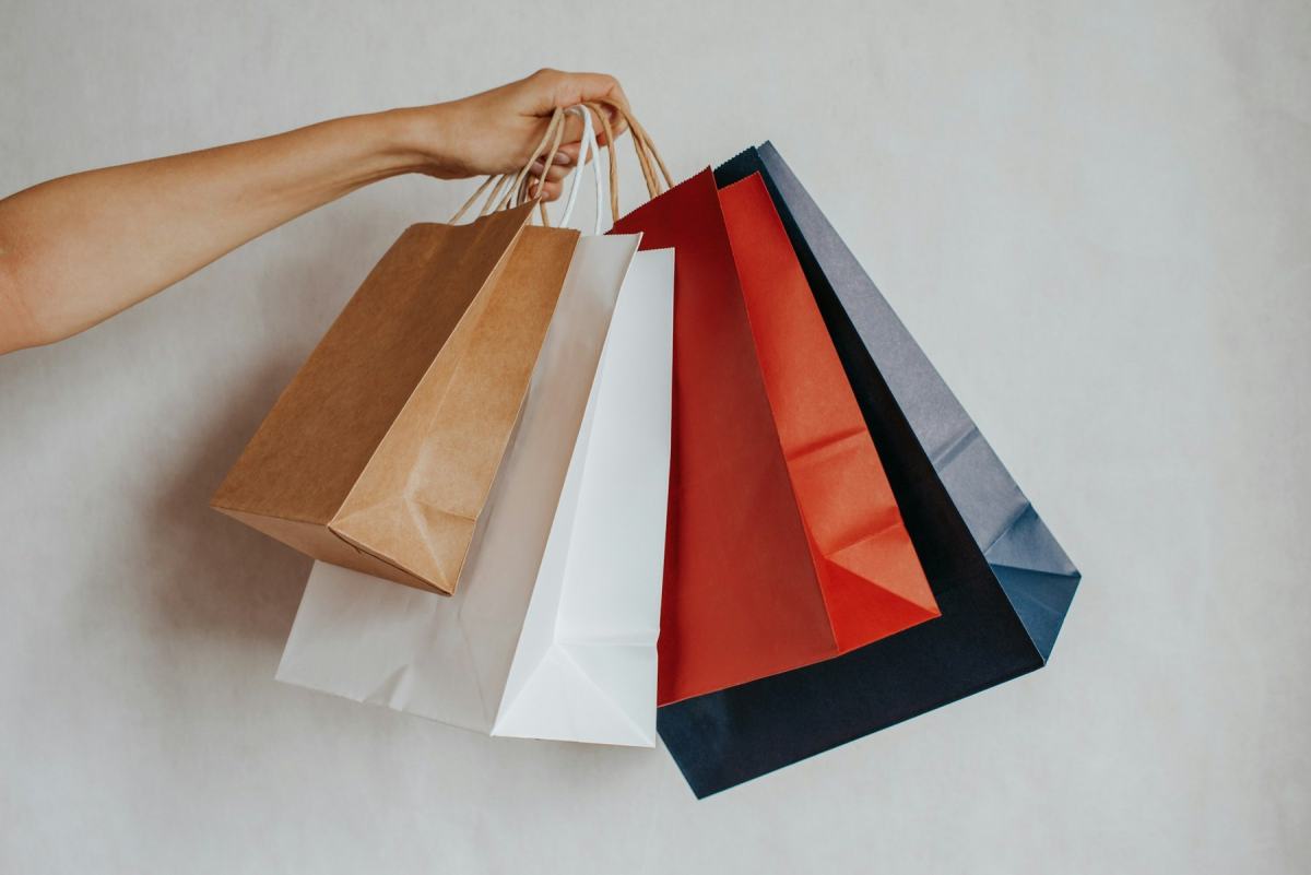 Hand hält mehrere Einkaufstüten aus Papier in Braun, Weiß, Rot und Schwarz