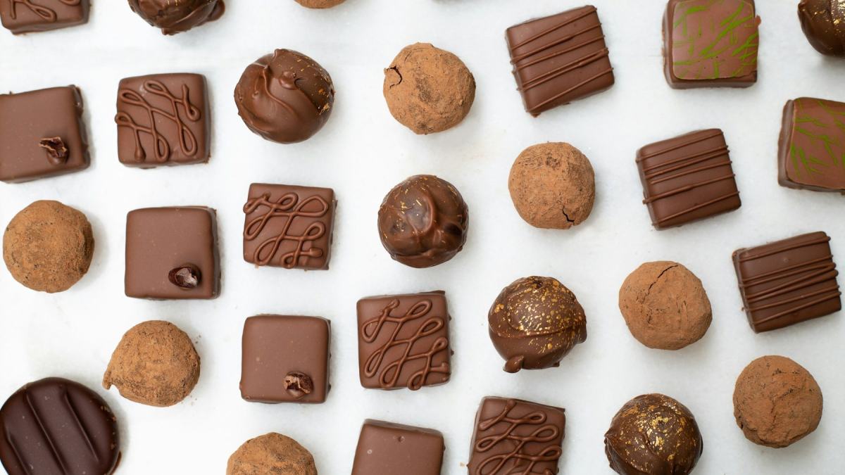 Pralinen und kleine Schokoladentäfelchen in Reihen auf weißem Grund
