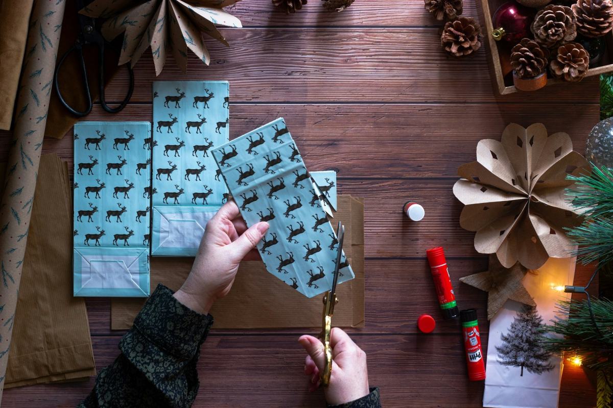 Hände schneiden Papiertaschen mit Rentiermuster für einen selbst gebastelten Adventskalender zu