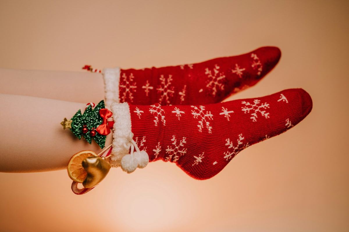 Beine in roten Strick-Socken mit Schneeflockenmuster und einem kleinen Weihnachtsanhänger