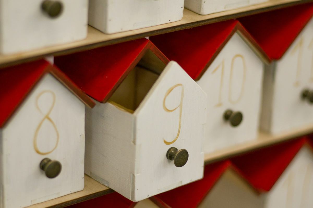 Adventskalender aus weißen Holzhäuschen mit roten Dächern und Messingknöpfen, das Türchen mit der 9 steht offen